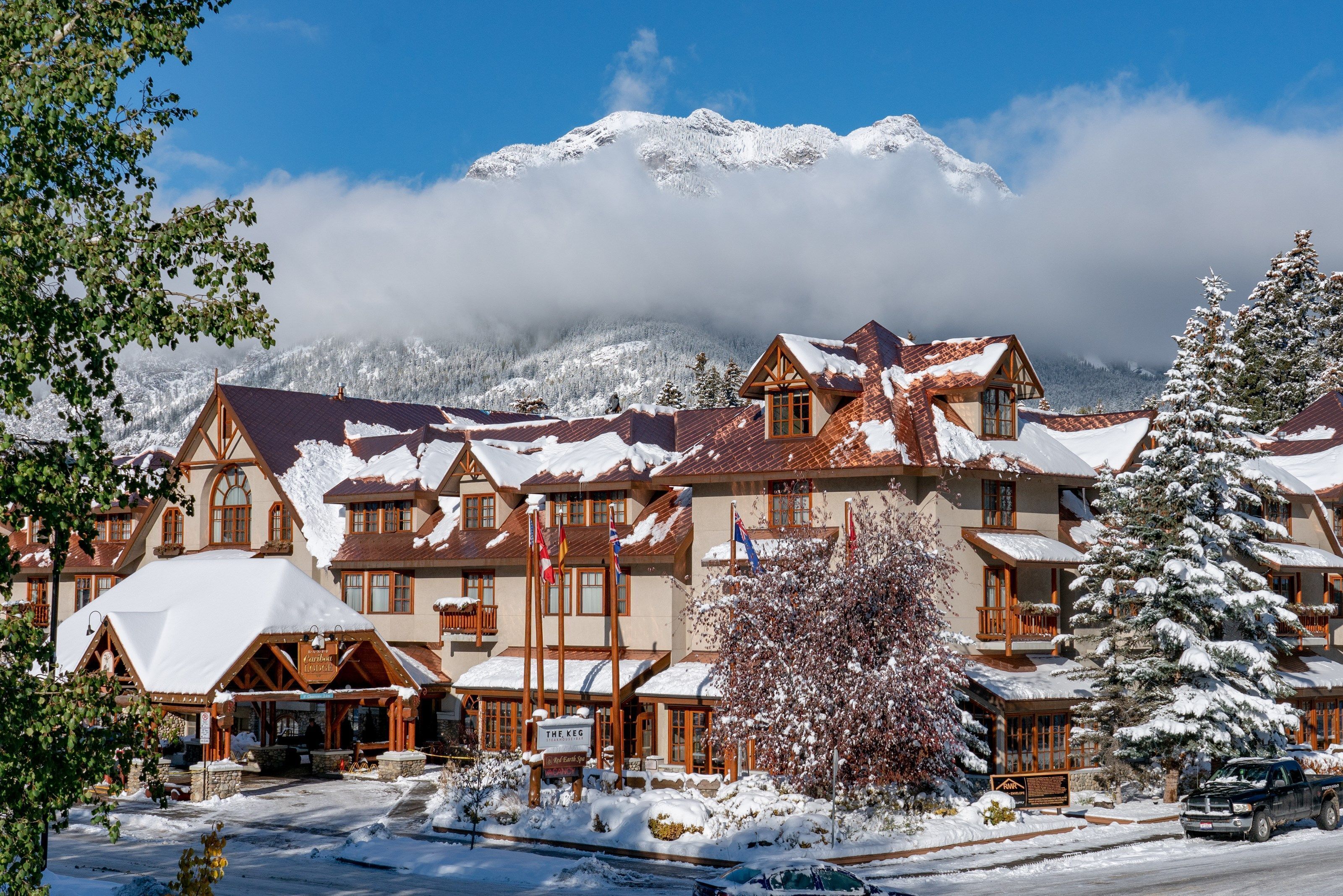 A snow-covered lodge with multiple buildings, a prominent sign, and a mountain backdrop.