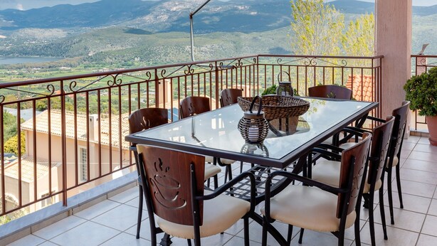 A balcony with a glass table and chairs, overlooking a mountainous landscape. - Fotis Apartment (Kefalonia)
