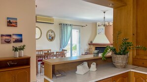 A kitchen with wooden cabinets, a marble countertop, and a dining area with a table and chairs. - Fotis Apartment (Kefalonia)