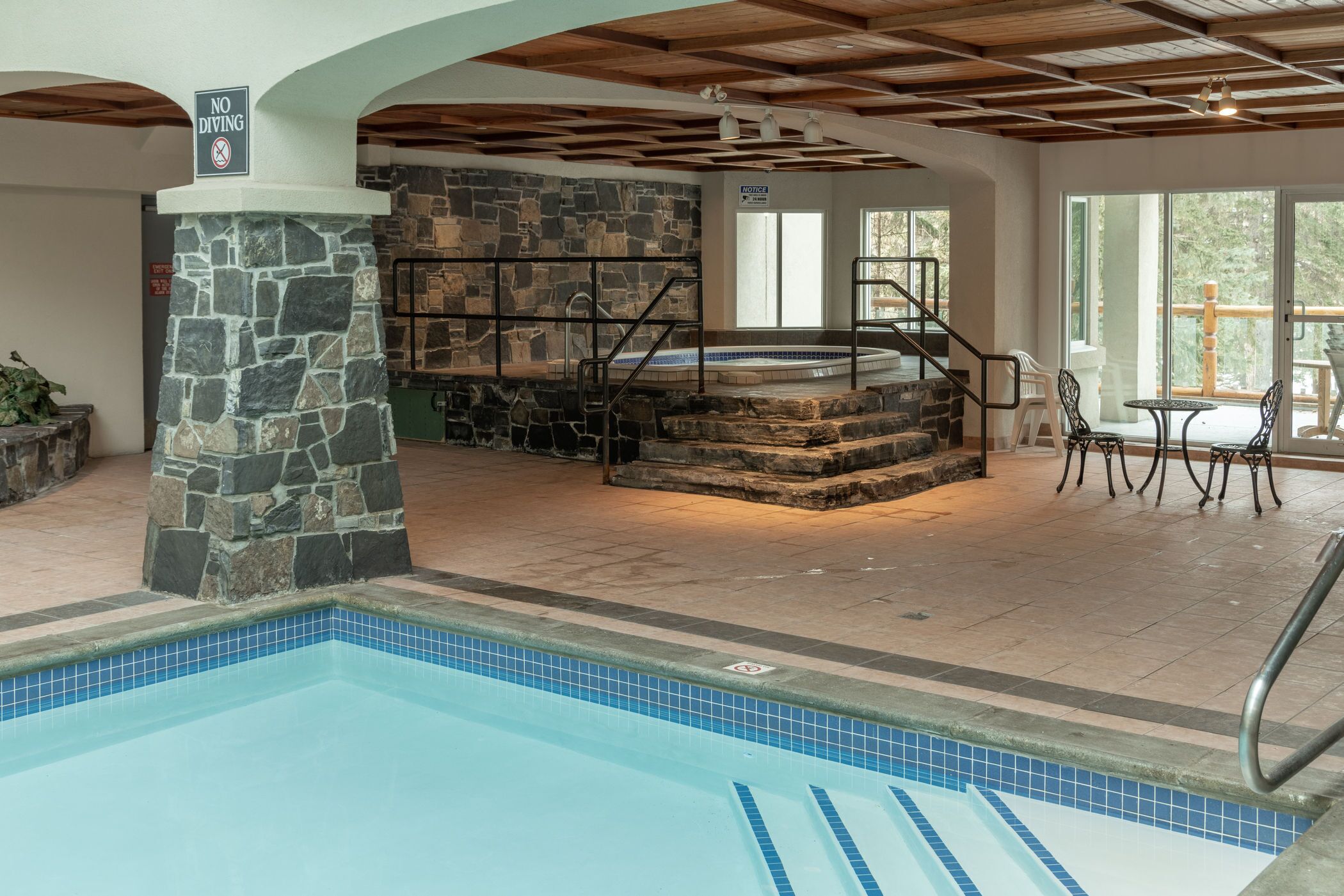 Un espace piscine agrémenté d’un mur en pierre, d’un jacuzzi et d’un escalier menant à un balcon.