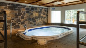 A hot tub with stone walls and wooden beams, a sign indicating a notice, and a view through large windows. - Relaxing Stay in Banff! Lovely Superior King Room (Banff)