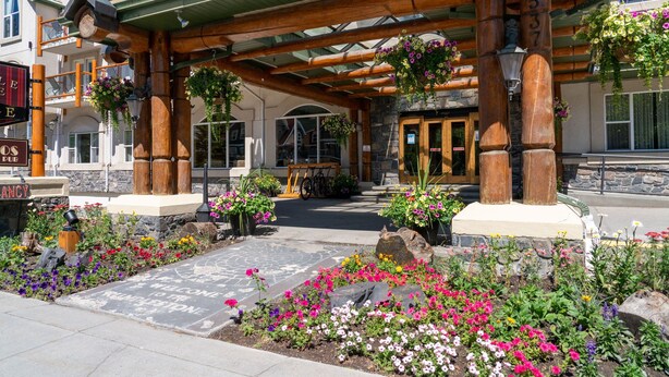A building with a wooden facade, a stone entrance, and a flower garden in front. - King Suite with Jetted Tub + Gas Fireplace (Banff)