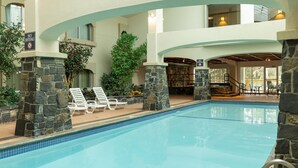 An indoor swimming pool with stone pillars, lounge chairs, and a view of the interior. - King Suite with Jetted Tub + Gas Fireplace (Banff)