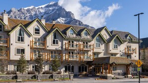 A multi-story hotel with a mountain backdrop, balconies, and a sign indicating a new establishment. - King Suite with Jetted Tub + Gas Fireplace (Banff)