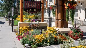 A sign for the Rundle Stone Lodge with a 'VACANCY' sign below it, surrounded by a flower bed. - King Suite with Jetted Tub + Gas Fireplace (Banff)