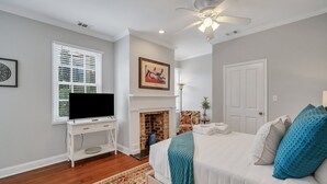 Un dormitorio con una cama, un televisor sobre un mueble, una chimenea y un ventilador de techo.