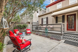 A backyard with outdoor seating, a wooden deck, and a house with a red door.