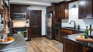 A modern kitchen with dark wooden cabinets, stainless steel appliances, and a granite countertop. - New! The Sanctuary House w/mountain view sleeps 14 (Medicine Park)