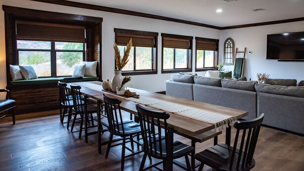 A dining area with a wooden table and chairs, a window seat with cushions, and a grey sofa. - New! The Sanctuary House w/mountain view sleeps 14 (Medicine Park)
