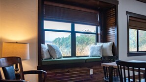 A cozy seating area with a bench, cushioned chairs, and a table, featuring a window with a view of trees. - New! The Sanctuary House w/mountain view sleeps 14 (Medicine Park)