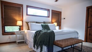 A bedroom with a large bed, bedside tables, a bench, and two windows with blinds. - New! The Sanctuary House w/mountain view sleeps 14 (Medicine Park)