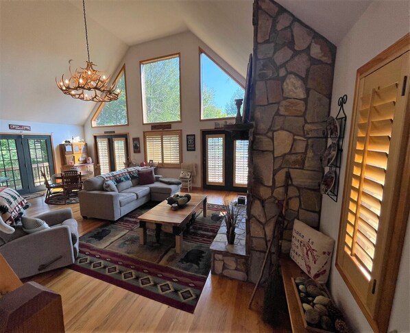 A spacious living room with a stone fireplace, large windows, and a chandelier. - Jolly Rancher Mountain Cabin (Murphy)