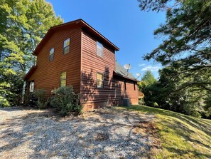 A two-story wooden cabin with a gravel driveway and surrounding trees. - Jolly Rancher Mountain Cabin (Murphy)