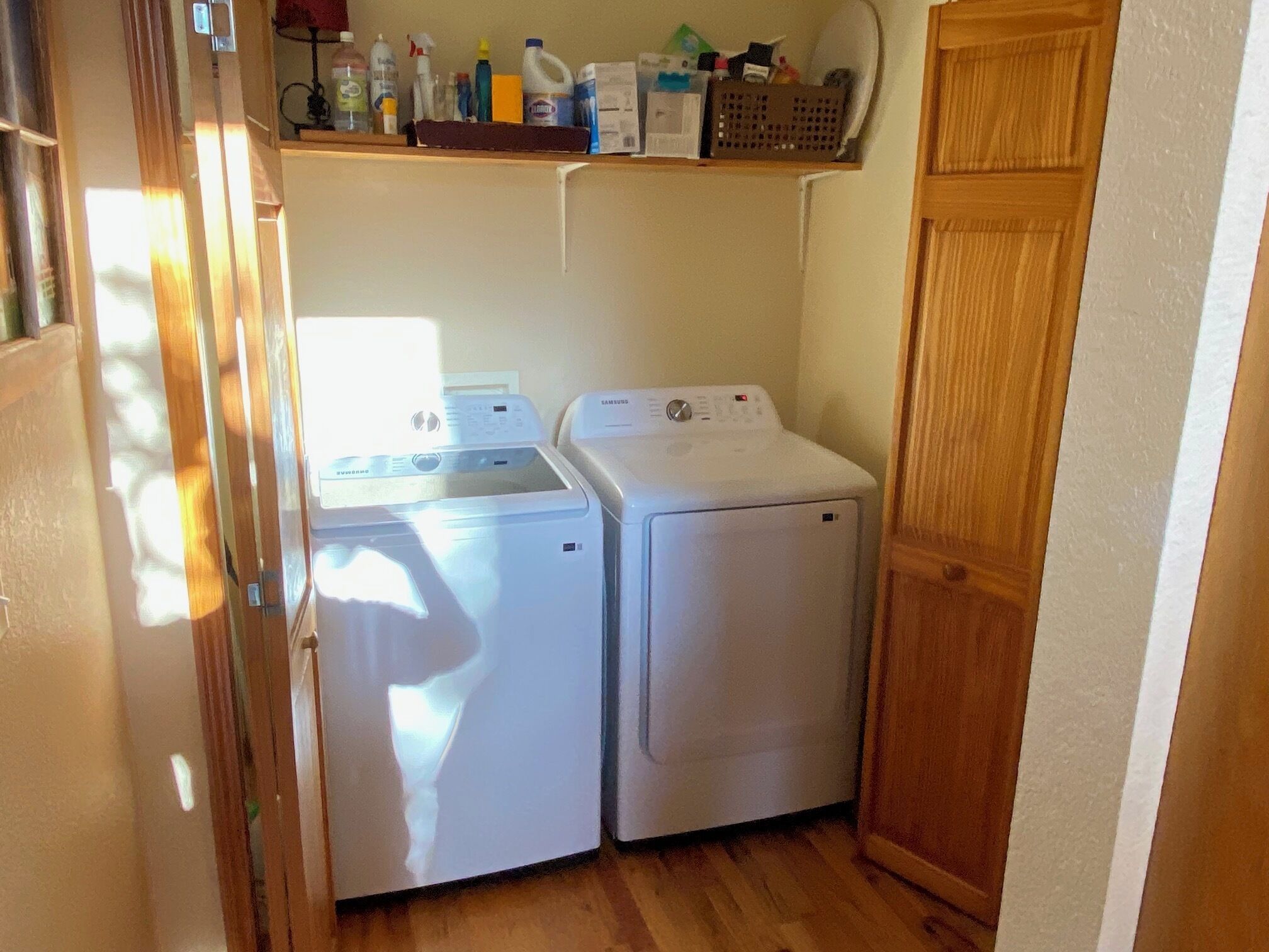 A laundry area with two white washing machines, a shelf with cleaning supplies, and a wooden door.