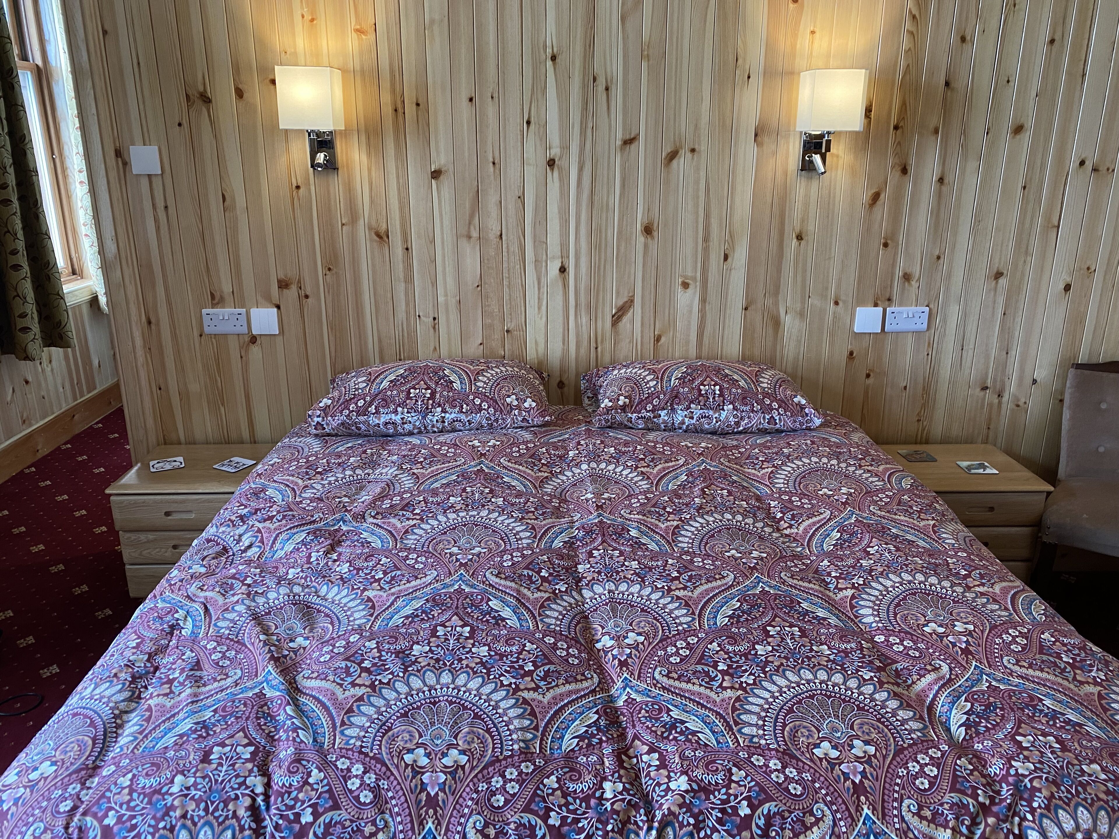 A double bed with a patterned bedspread, two bedside lamps, and a wooden headboard.