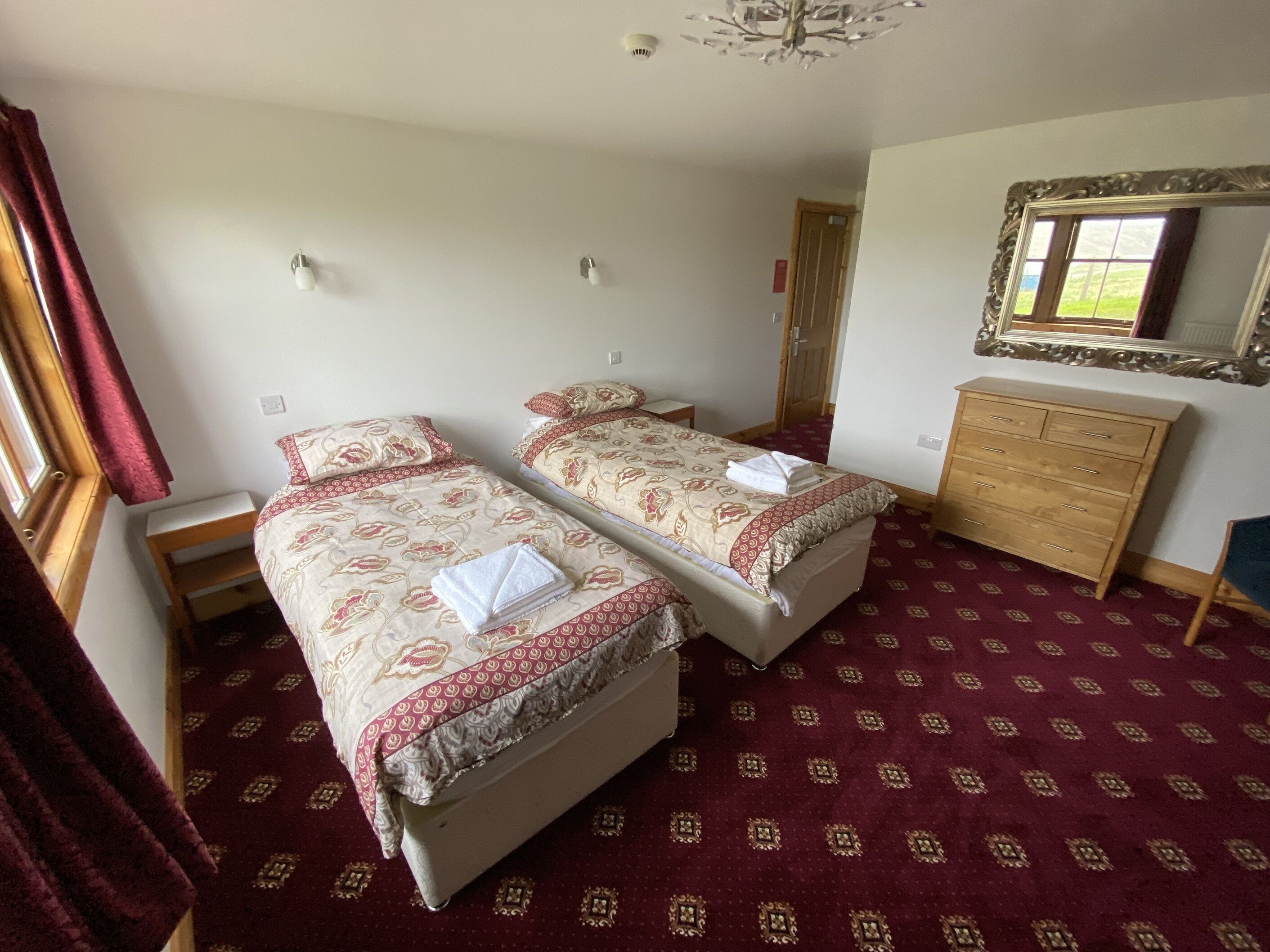 A hotel room with two beds, a wooden dresser, a mirror, and a patterned carpet.