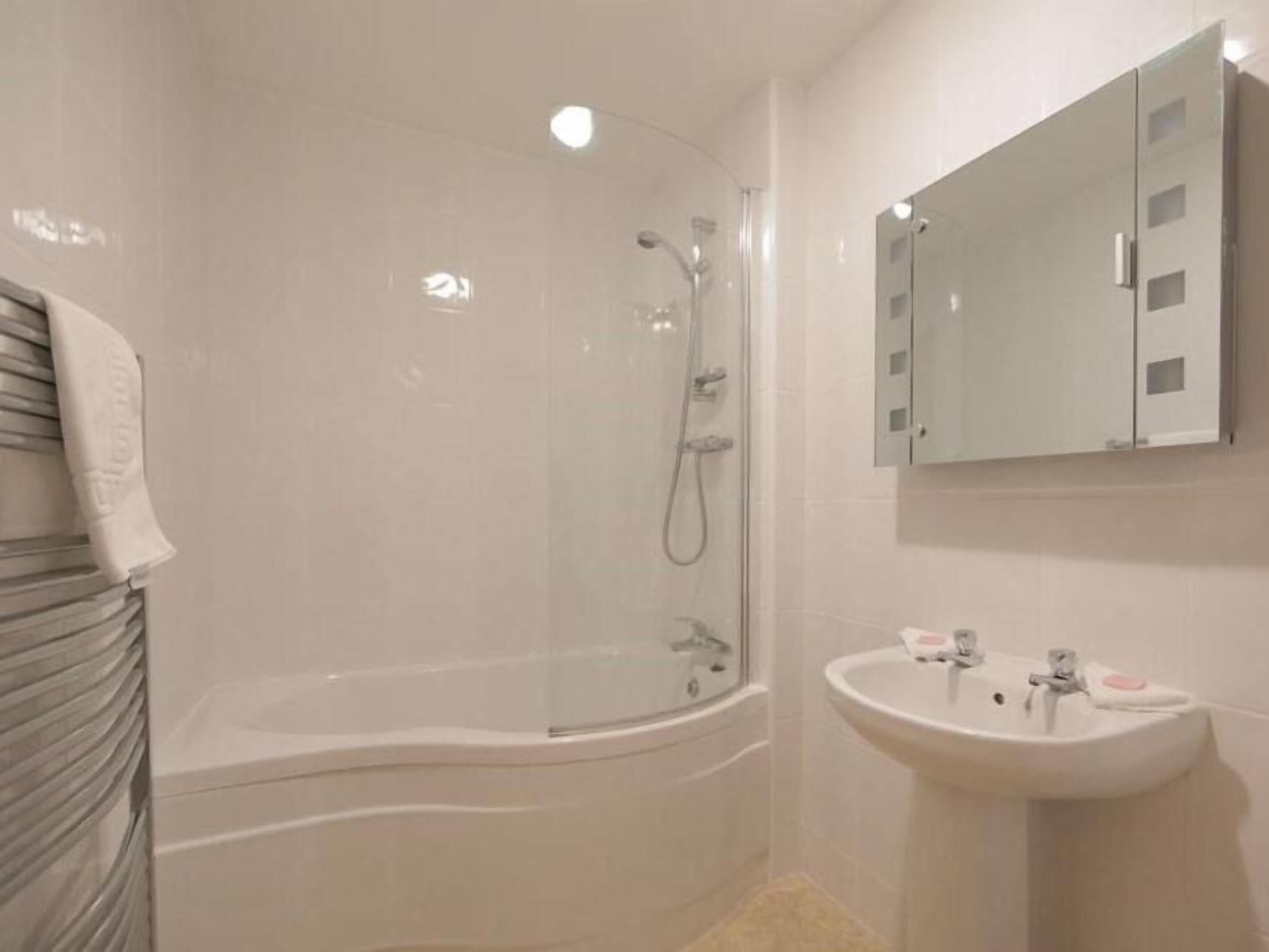 Un baño moderno con ducha envuelta en vidrio, bañera independiente y lavamanos sobre pedestal.