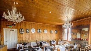 A wooden-paneled dining room with tables set for a meal, chandeliers, and a stone fireplace. - St Magnus Bay Hotel (Hillswick)