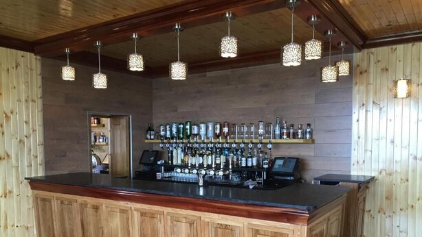 A bar area with wooden paneling, a counter with a cash register, and hanging pendant lights. - St Magnus Bay Hotel (Hillswick)