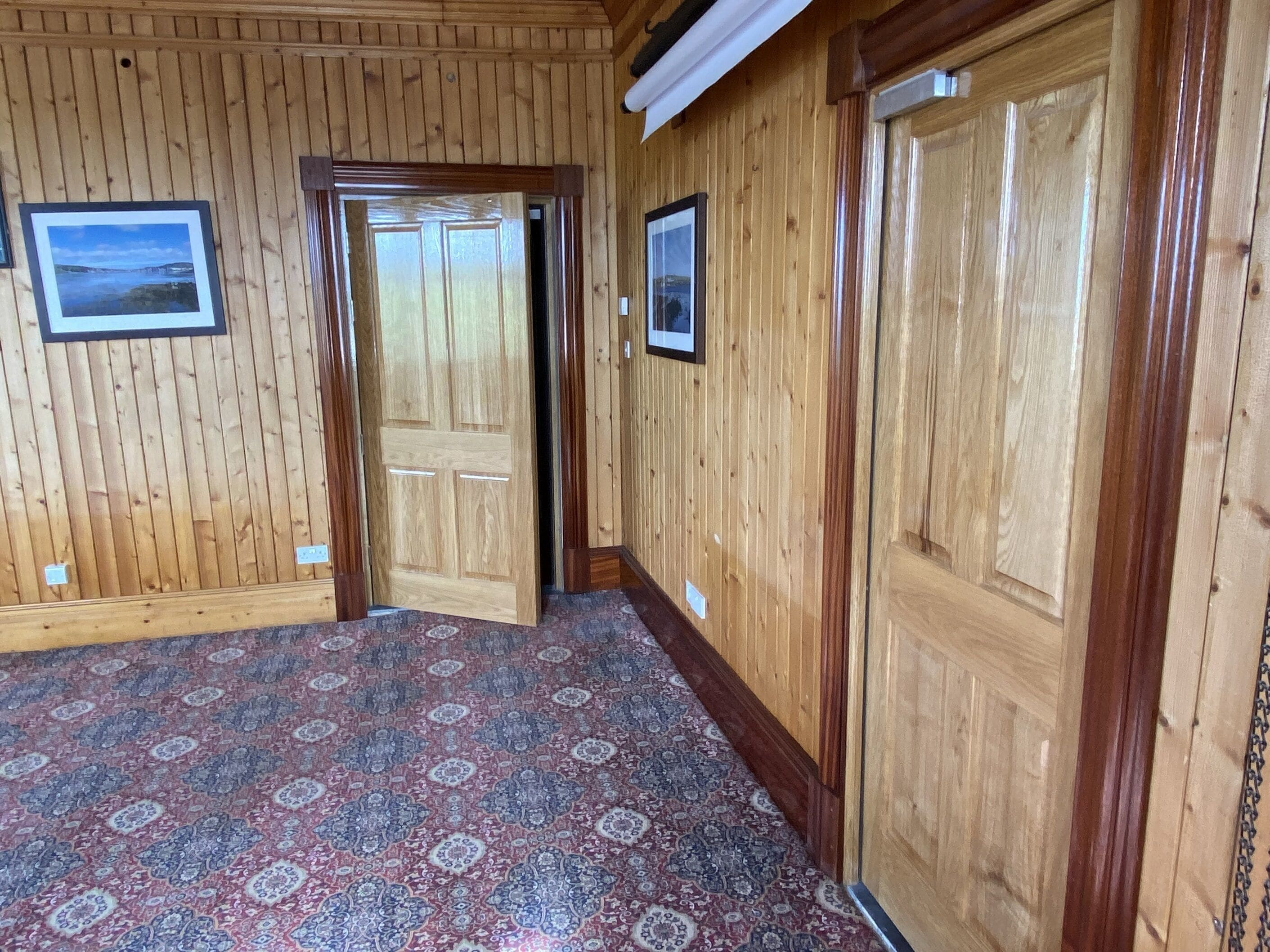 A hallway with wooden paneling, patterned carpet, and two doors.