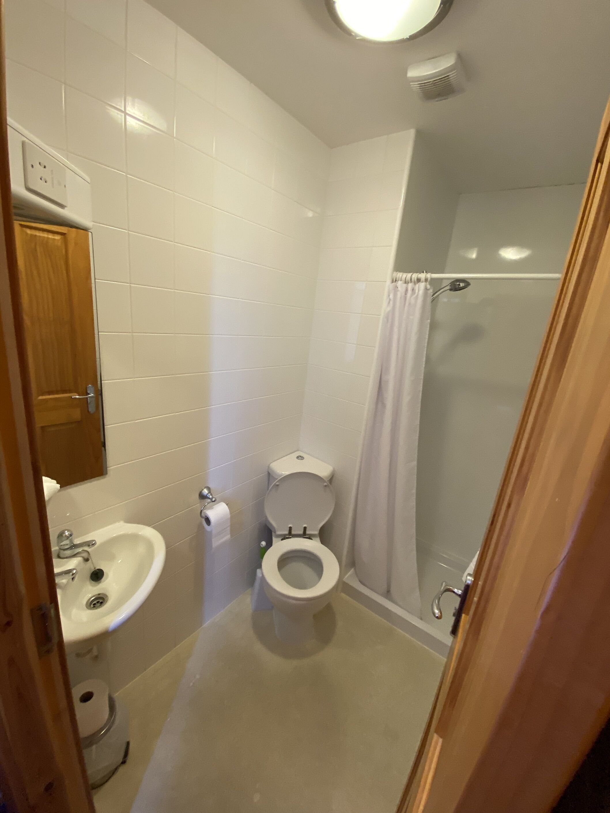 Un baño pequeño con azulejos blancos, un inodoro, un lavabo y una ducha.