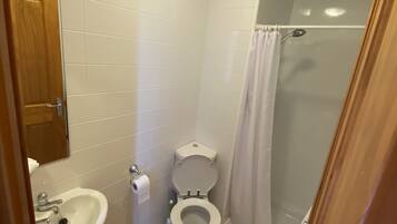 Un baño pequeño con azulejos blancos, un inodoro, un lavabo y una ducha.