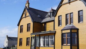 A yellow two-story house with a gabled roof, multiple windows, and a front porch. - St Magnus Bay Hotel (Hillswick)