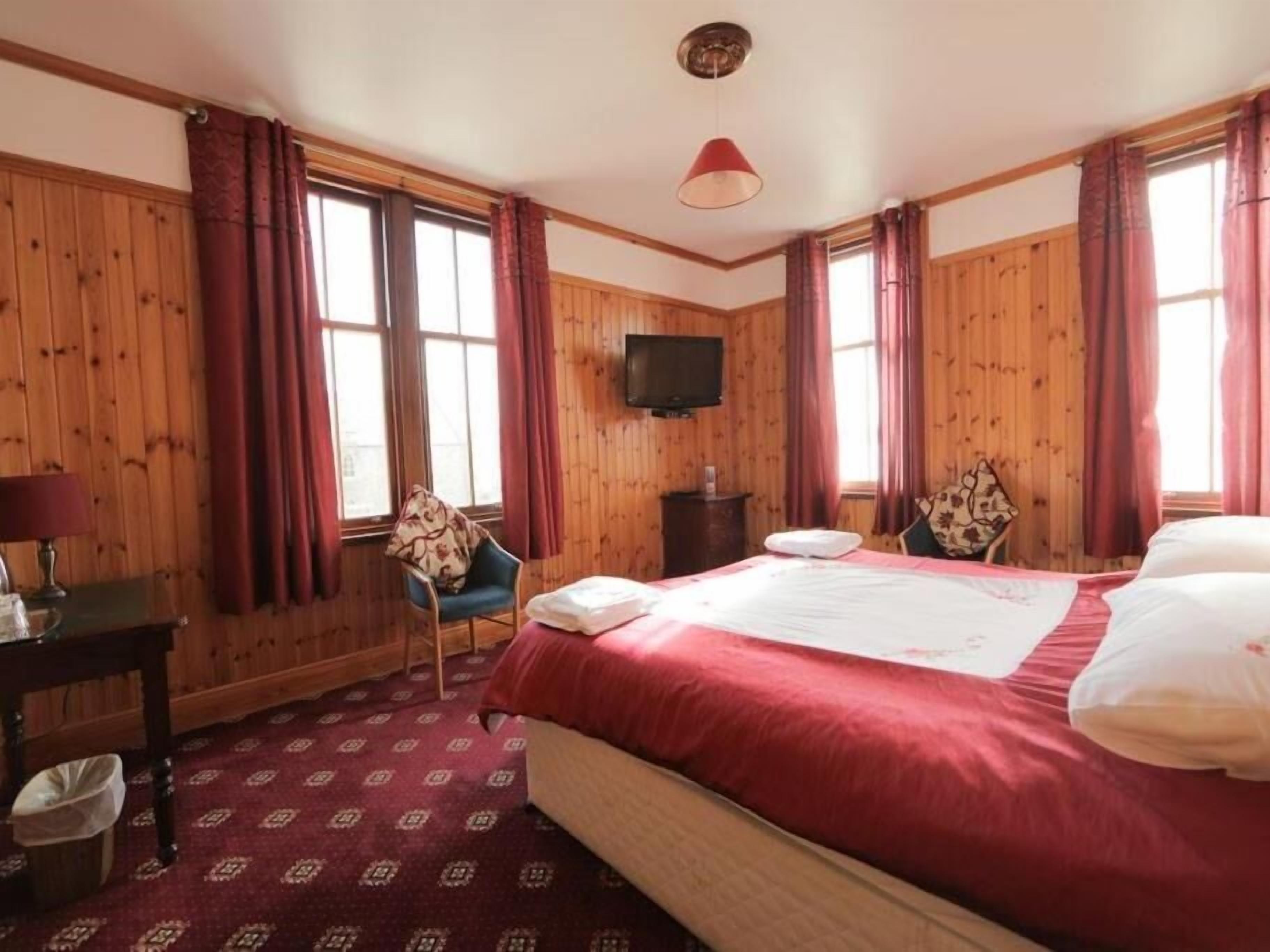 Habitación de hotel con una cama grande, paredes de madera, televisión y una ventana con cortinas.