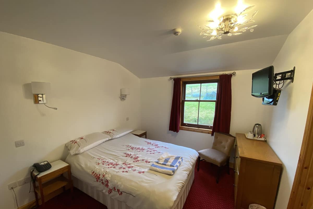 A bedroom with a bed, a desk, a chair, a television, and a window with curtains.