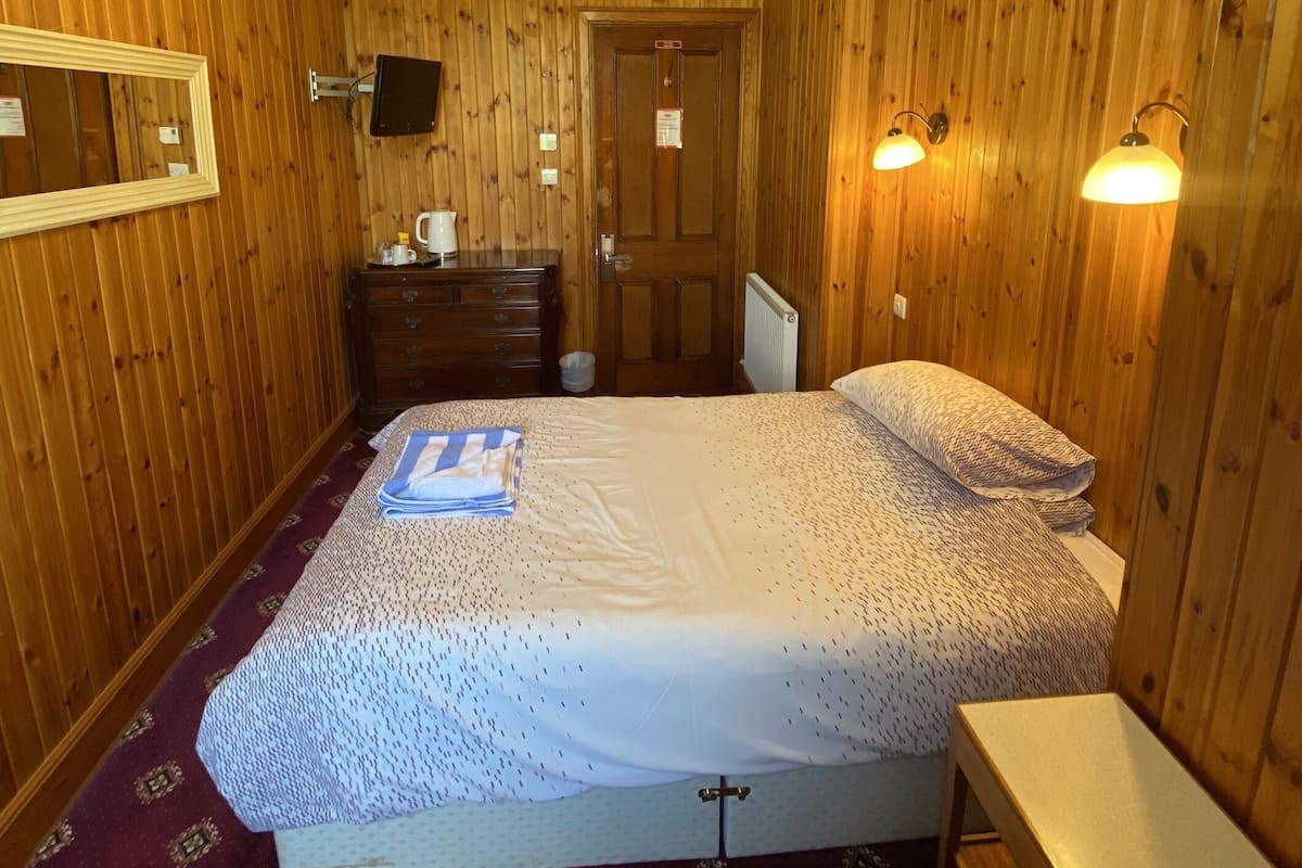 A wooden-paneled bedroom with a bed, bedside table, dresser, and a mirror.