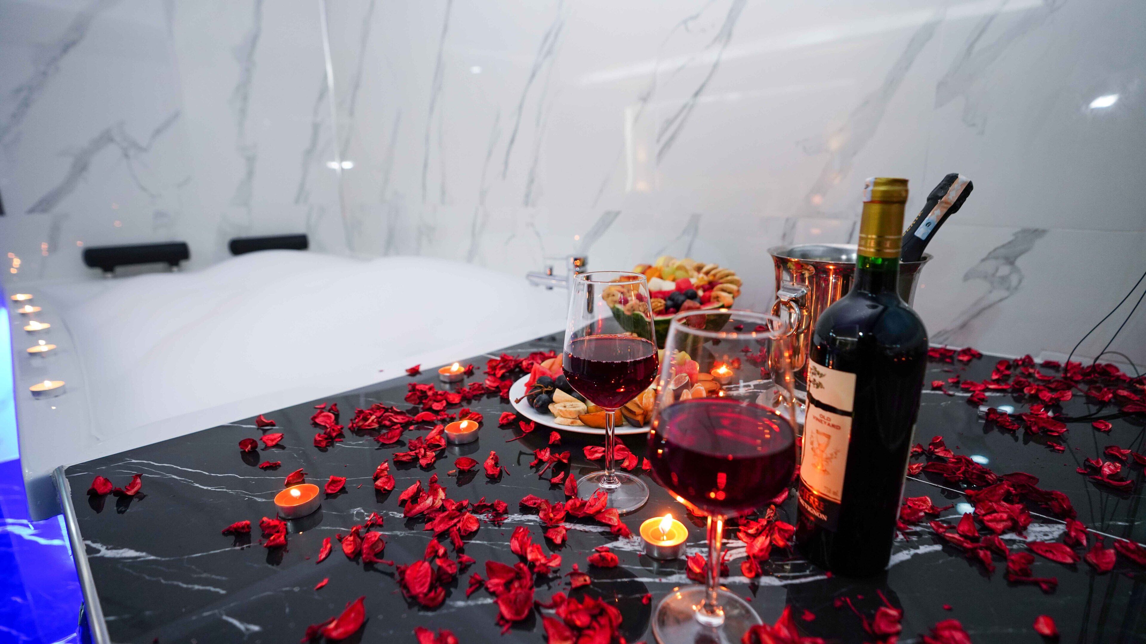 A table set with a bottle of wine, glasses, a plate of food, and candles.