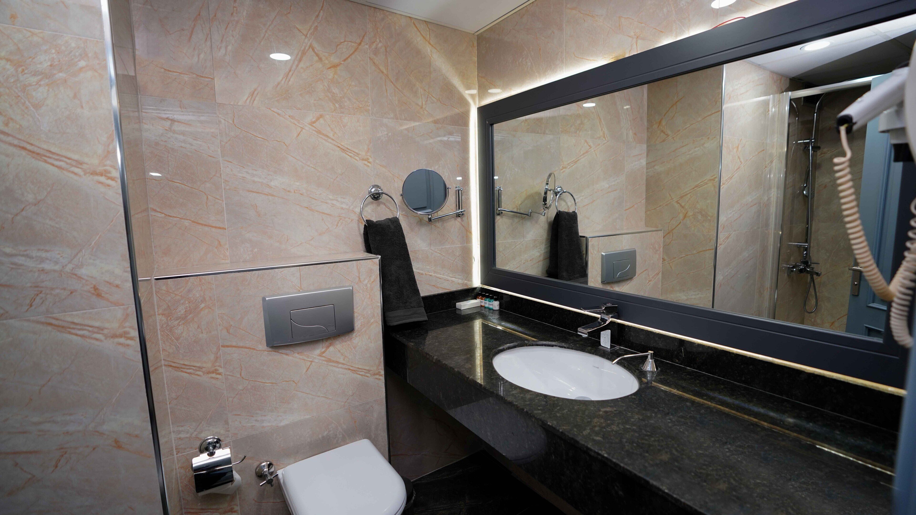 A modern bathroom with a marble floor, a large mirror, a sink, and a toilet.