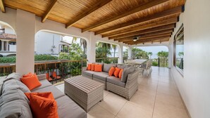 A covered outdoor seating area with a wooden ceiling, a gray sofa with orange cushions, and a wicker coffee table. - Villa Potrero Luxury Private Beachfront Home with Housekeeper, Concierge (Provincia de Guanacaste)