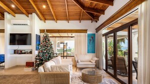 A spacious living room with a wooden ceiling, a large Christmas tree, a flat-screen TV, and a view of the outdoors through large sliding glass doors. - Villa Potrero Luxury Private Beachfront Home with Housekeeper, Concierge (Provincia de Guanacaste)