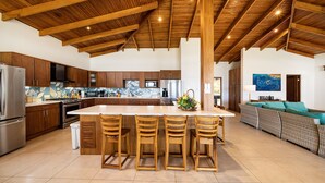 A spacious kitchen with wooden beams, a central island with bar stools, and a living area with a sofa and a 'WELCOME' sign. - Villa Potrero Luxury Private Beachfront Home with Housekeeper, Concierge (Provincia de Guanacaste)