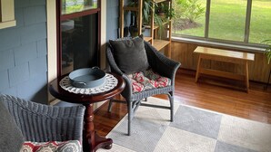 A cozy room with a ceiling fan, wicker furniture, a wooden bench, and a view of a green lawn through large windows. - Cozy Private home (Warrensburg)