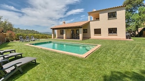 Una casa de dos pisos con piscina, un patio cubierto y un césped bien cuidado.