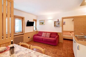 A cozy room with a wooden table, a red sofa, a TV, and a kitchen area.