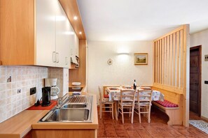 Une cuisine compacte équipée d’un évier, d’une cuisinière et de meubles de rangement en bois. Un coin repas avec une table et des chaises est situé à côté de la cuisine.