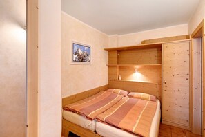 A bedroom with a wooden bed, a wooden wardrobe, and a shelf unit.
