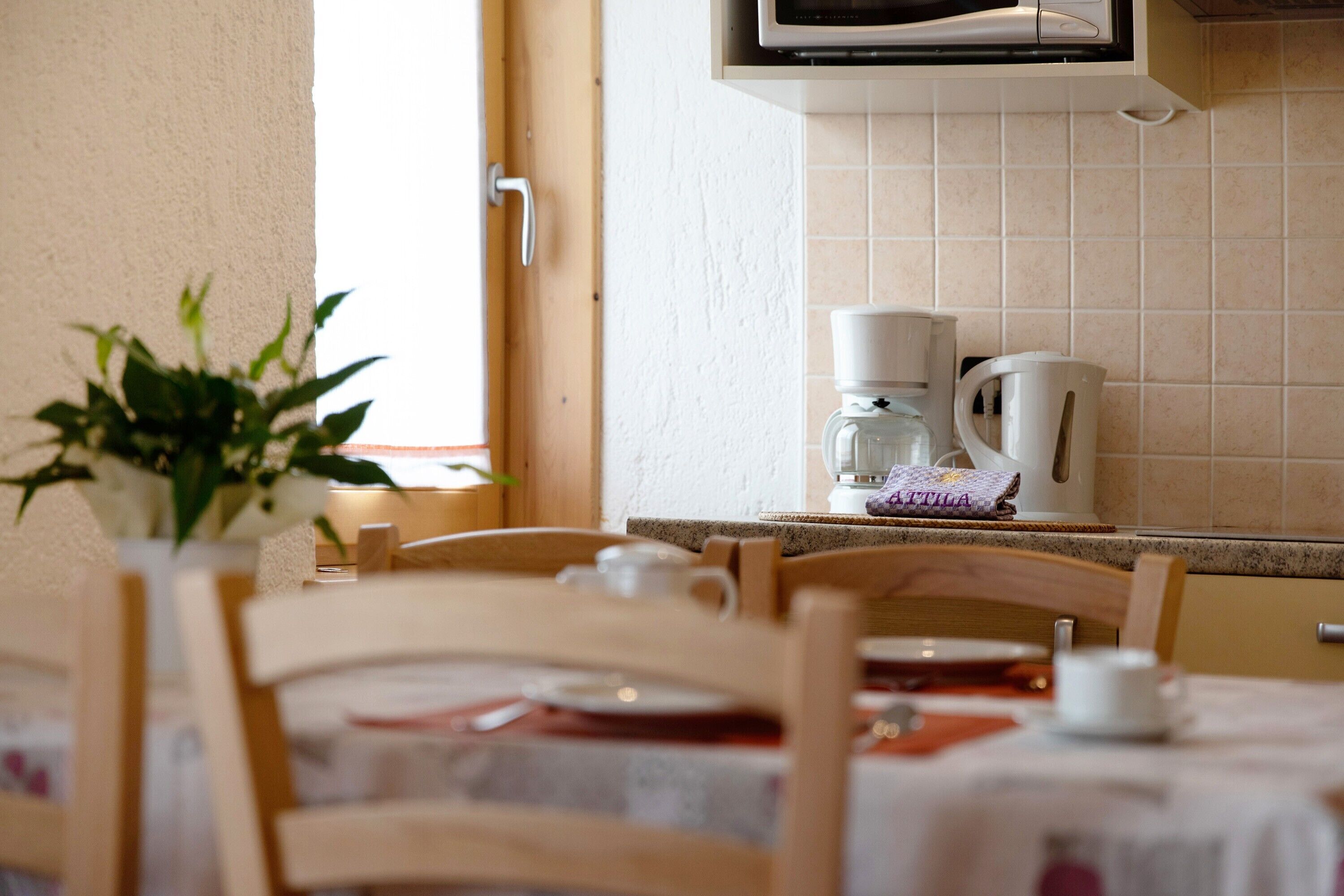 A kitchen with a microwave, coffee maker, and a window with a plant.