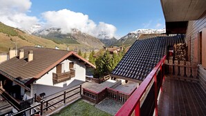 Un chalé con balcón de madera, patio de piedra y vista a la montaña.