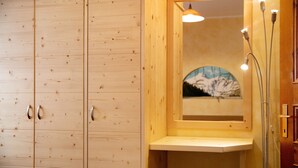 Interior de una cabaña de madera con un armario de madera, un pequeño banco y un cuadro enmarcado de una montaña nevada.