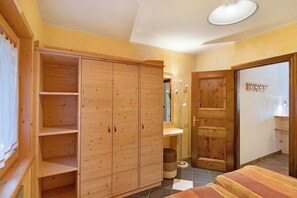 Une chambre à coucher avec un lit, une armoire en bois et une salle de bain équipée d’un miroir et d’un lavabo.