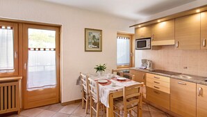 Una cocina compacta con armarios de madera, una mesa de comedor con sillas, un microondas y una ventana con cortinas.