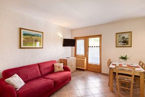 Un canapé rouge, une table à manger en bois et un téléviseur fixé au mur.