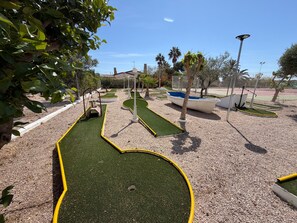 Ein Minigolfplatz mit grünem Kunstrasen, gelben Rändern und einigen Palmen.