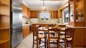 A kitchen with wooden cabinets, a stainless steel refrigerator, a dining table with chairs, and a window with a view. - Apartment 'Christine's House' with Private Pool, Wi-Fi and Air Conditioning (Zakynthos)