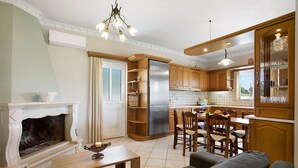 A modern kitchen with wooden cabinets, a built-in refrigerator, and a dining area with chairs and a table. - Apartment 'Christine's House' with Private Pool, Wi-Fi and Air Conditioning (Zakynthos)
