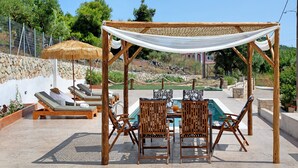 A poolside area with lounge chairs, a table, and a pergola with a white canopy. - Apartment 'Christine's House' with Private Pool, Wi-Fi and Air Conditioning (Zakynthos)